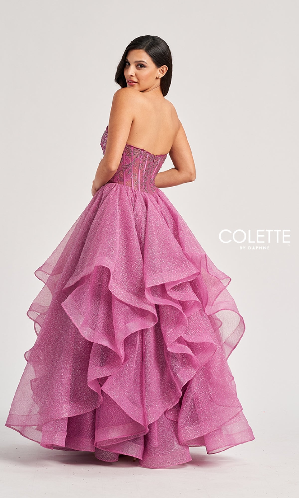 A woman wears the Long Prom Ball Gown: Colette CL8200, featuring a strapless beaded corset bodice and a ruffle-tiered glitter tulle skirt. Against a plain background, the fitted top and voluminous layers create a dazzling prom look.